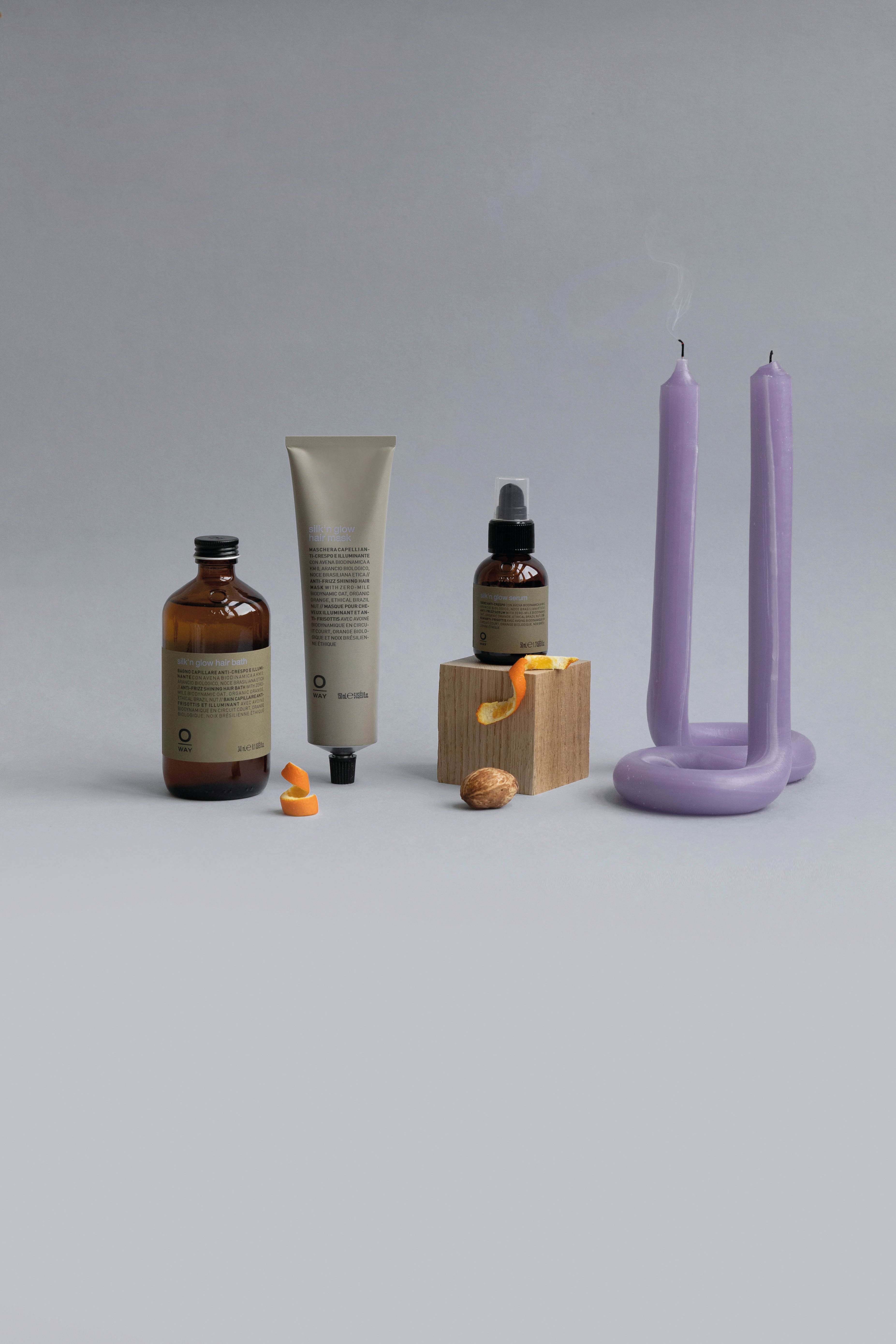 Three skincare items, a wooden block with orange peel, a walnut, and a lavender U-shaped candle sit on a gray surface—perfect inspiration for Oway Silk’N Glow Hair Bath, a taming hair bath for frizz-prone hair by Oway.
