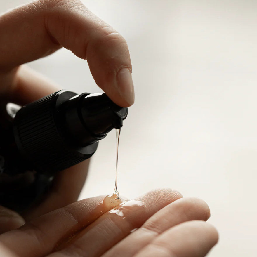 A hand dispenses Oway Silk’N Glow Serum, an anti-frizz shine serum for dry, frizzy hair, enriched with Brazil nut oil, from a black bottle onto the palm of the other hand.