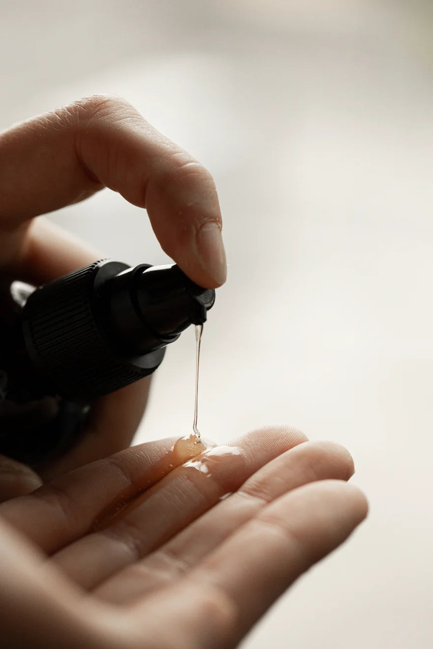 A hand dispenses Oway Silk’N Glow Serum, an anti-frizz shine serum for dry, frizzy hair, enriched with Brazil nut oil, from a black bottle onto the palm of the other hand.