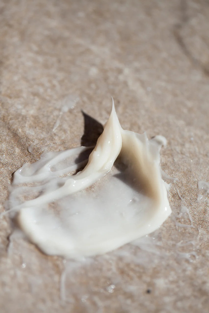 A close-up of Oway Silk’N Glow Hair Mask, a white nourishing mask for dry, frizzy hair, spread on a beige textured surface—perfect for smoother, healthier-looking hair.