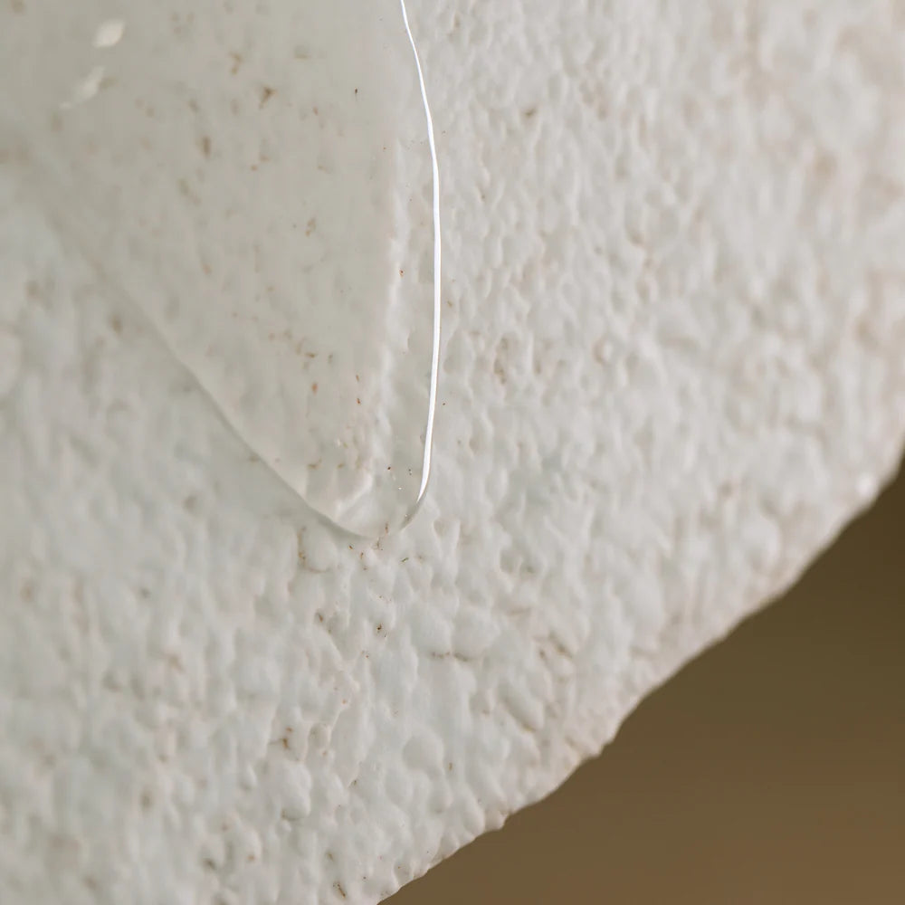 Close-up of a clear liquid drop on textured white, highlighting both the fluid and surface—perfect for showcasing Oway Curly Hair Bath, a sulfate-free cleanser by Oway designed for wavy and curly hair.