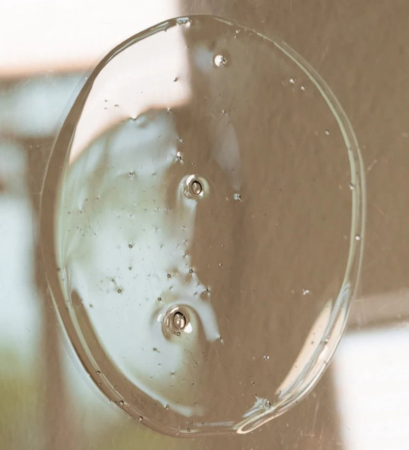 A close-up of Oway Silk’N Glow Hair Bath, a clear gel with tiny bubbles, spread in a circle on a reflective surface—perfect for taming frizzy hair and boosting the effects of your smoothing shampoo.