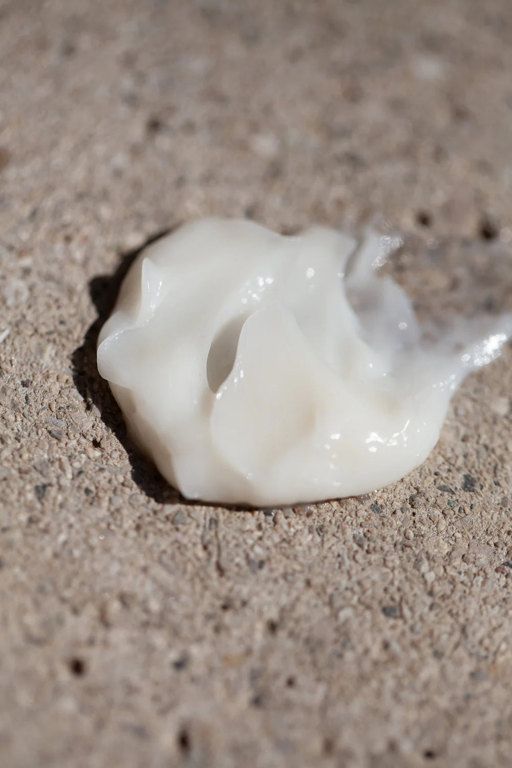 A dollop of Oway Curl Priming Cream | Moisture-Rich Curl Primer for Frizz-Free Styling is spread on a rough, textured beige surface, showcasing its rich hydration.