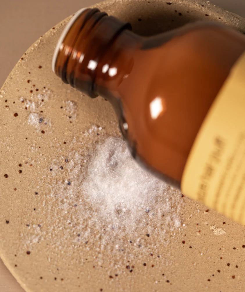 Oway Volume and Texture Hair Puff, a Volumizing Styling Powder by Oway, is shown pouring from a brown glass bottle onto a speckled beige ceramic plate—ideal for adding instant lift and volume to fine hair.