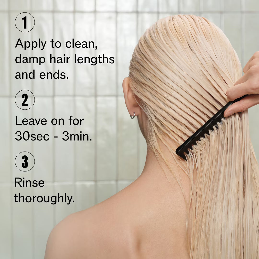 Person applying a product to their hair with a comb, set against a tiled shower wall.