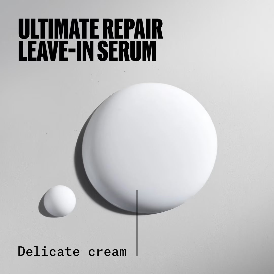 Two droplets of a white serum with text 'Ultimate Repair Leave-In Serum' and 'Delicate cream' on a gray background.