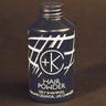 A blue bottle of Cult and King PUMPABLE HAIR POWDER, an antioxidant-rich, talc-free dry shampoo with white text and design, stands against a dark background.