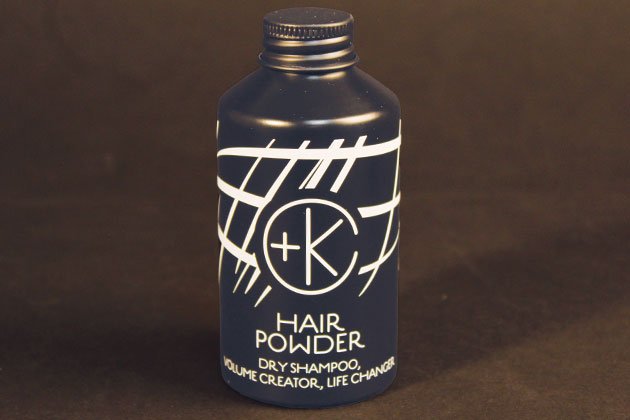 A blue bottle of Cult and King PUMPABLE HAIR POWDER, an antioxidant-rich, talc-free dry shampoo with white text and design, stands against a dark background.
