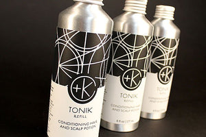Three silver Cult and King TONIK Conditioning Hair & Scalp Potion bottles with black and white geometric labels are shown: two stand upright (hair conditioner), while one (scalp tonic) sits behind them with the cap off.