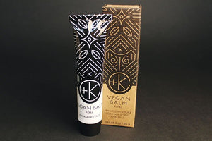 A black-and-white tube labeled “Cult and King VEGAN BALM | Manifest Moisture for Hair Styling and Face” stands by its matching geometric-patterned box; this refill styling balm contains botanical oils for hair and face.