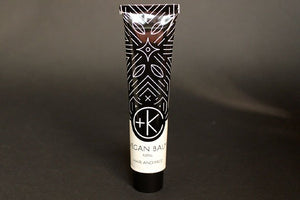 A tube of Cult and King VEGAN BALM | Manifest Moisture for Hair Styling and Face stands upright against a plain dark background. The black, white, and beige tube features geometric patterns and nourishing botanical oils.