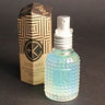 A textured glass spray bottle filled with a light blue liquid, enriched with Malachite Extract, stands beside a geometric-patterned box featuring the Cult and King branding and labeled as "Cult and King SET SPRAY | NEW FORMULATION: Semi-Precious Tri-Phase Wonderworking Hairspray.
