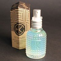A textured glass spray bottle filled with a light blue liquid, enriched with Malachite Extract, stands beside a geometric-patterned box featuring the Cult and King branding and labeled as "Cult and King SET SPRAY | NEW FORMULATION: Semi-Precious Tri-Phase Wonderworking Hairspray.