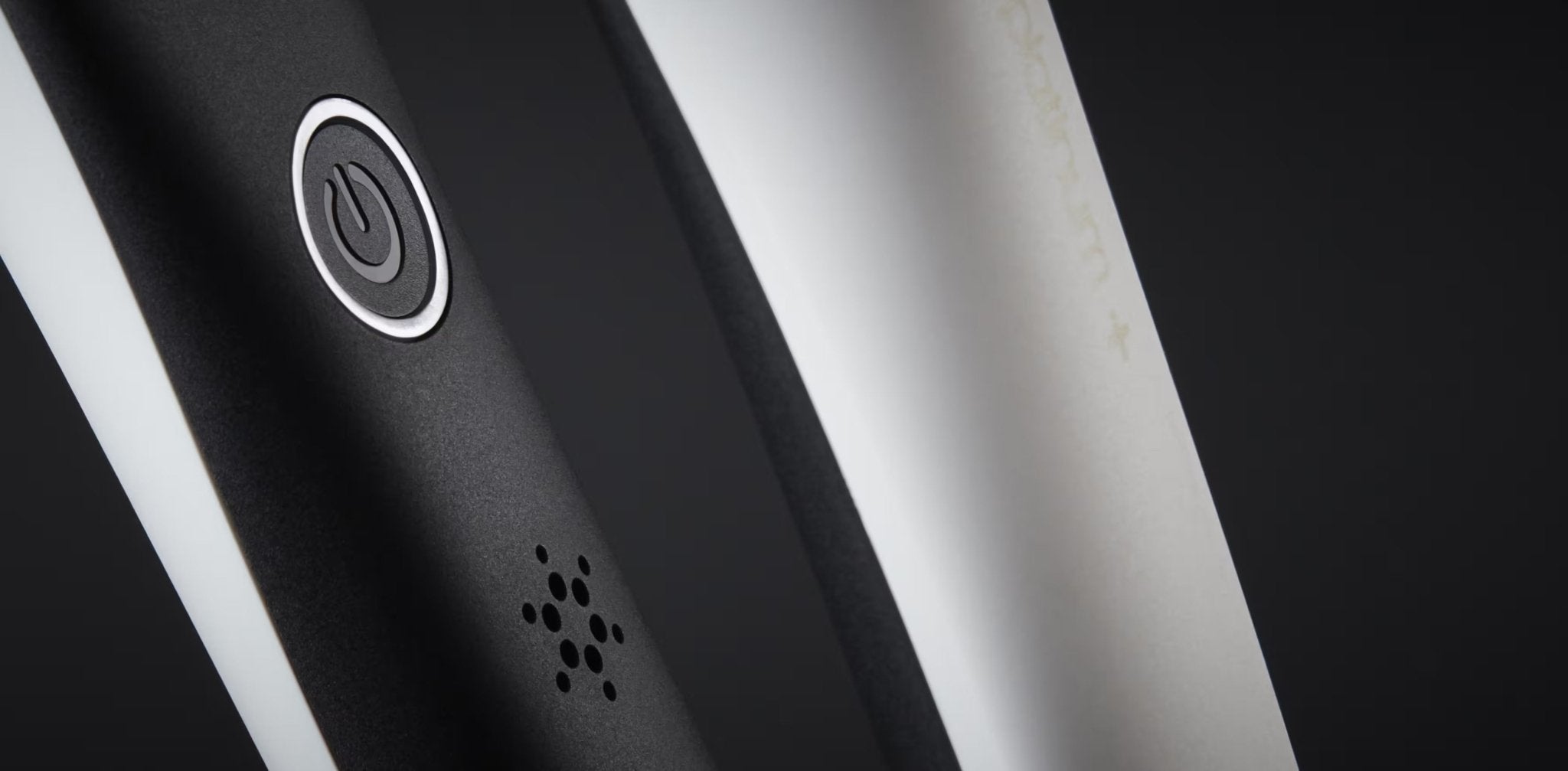 Close-up of the power button on a GHD PLATINUM+ STYLER - 1" FLAT IRON with a mesh vent underneath, positioned next to a white surface.