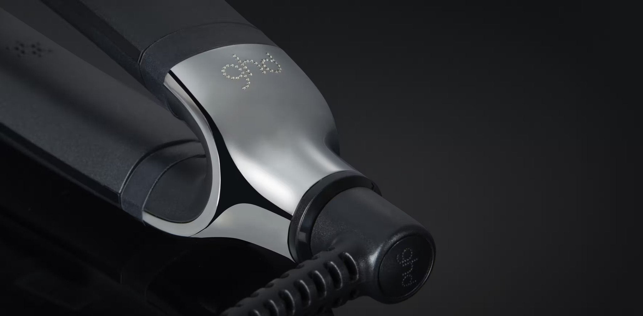 Close-up of a black and silver GHD PLATINUM+ STYLER - 1" FLAT IRON against a dark background, perfect for achieving flat iron waves.