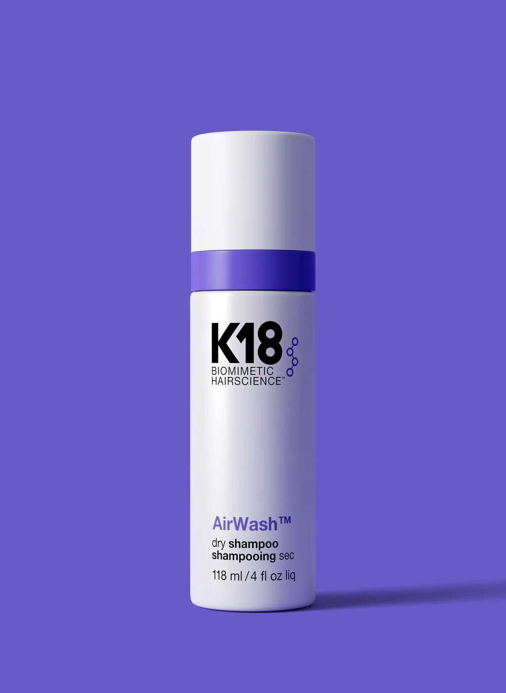 A cylindrical white bottle with a purple stripe, labeled "K18 AirWash Dry Shampoo," stands against a solid purple background. Enhanced with odorBIND™ biotechnology, the bottle holds 118 ml (4 fl oz) and promotes scalp health.