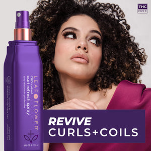 A woman with curly hair wearing a purple top looks to the side. In the foreground is a purple bottle of Leaf and Flower Instant Curl Refresh Spray by Leaf and Flower, featuring vegan polymers and text that reads, "Revive Curls + Coils.