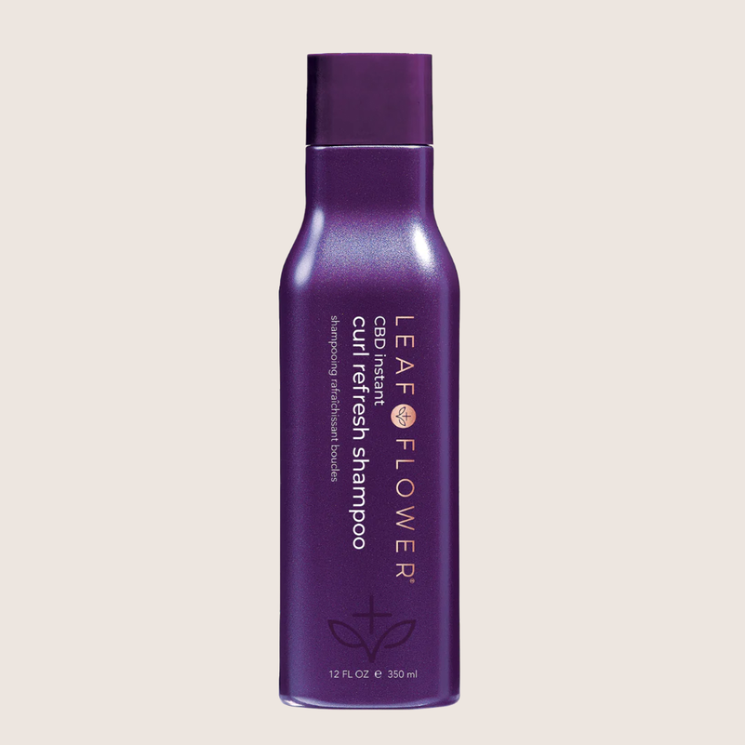 A purple Leaf and Flower Instant Curl Refresh Shampoo bottle with white text is set against a light backdrop. This vegan, color-safe formula enhances vibrant, healthy curls with every wash.