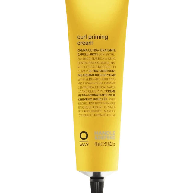 A yellow tube of Oway Curl Priming Cream | Moisture-Rich Curl Primer for Frizz-Free Styling with black text and a metallic cap is set against a textured green background. Its Marula Oil-infused details are printed in several languages on the packaging.