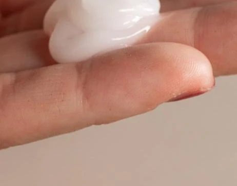 A close-up of fingers holding a dollop of Oway Frequent Use Conditioner, a lightweight formula for everyday use, against a neutral background.