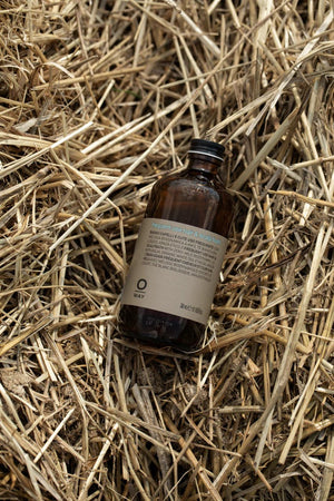 A brown Oway Frequent Use Hair & Scalp Bath bottle with a beige label rests on yellow straw. The artisanal packaging hints at its gentle daily shampoo formula, ideal for all hair types and crafted by Oway.