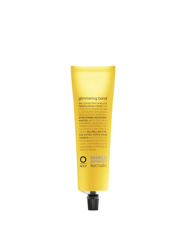 A yellow tube labeled "Oway Glimmering Bond | Bonding Shine Treatment for Damaged, Dull Hair" stands upright with a black cap, featuring product details about marula oil and other ingredients in multiple languages.