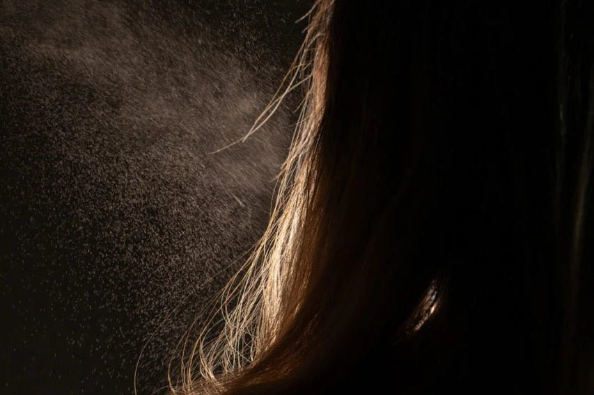 Oway Phytoprotein Mist, a leave-in treatment, is sprayed on the back of fragile, stressed hair, with visible droplets highlighted against a dark backdrop to showcase its plant-based protein strength.