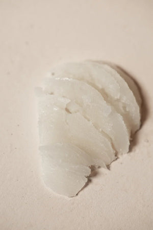 A close-up of Oway Precious Wax by Oway, featuring several oval slices with a translucent white, slightly waxy texture and luminous shine, arranged on a plain surface to showcase its natural definition and shine-enhancing qualities.