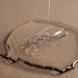 A close-up shows Oway Purifying Hair Bath for Oily Scalp, a transparent liquid forming bubbles on a beige surface—ideal for highlighting this organic Oway shampoo that effectively prevents dandruff and cares for oily scalps.
