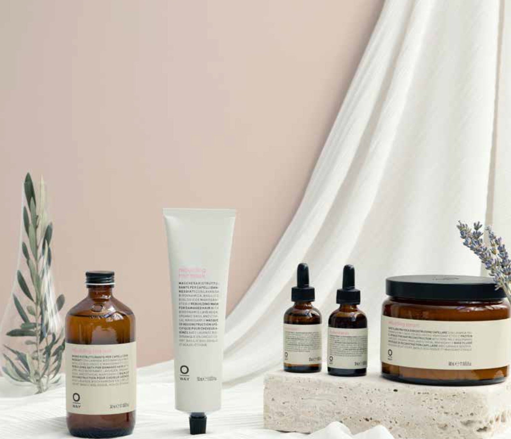 The Oway Rebuilding Hair Mask, a restorative mask for damage and instant repair, in amber packaging is displayed on light fabric with small plants and a textured stone.