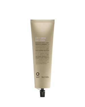 A beige tube of Oway Silk’N Glow Hair Mask for dry, frizzy hair, enriched with Organic Cupuaçu Butter. The upright tube has a black screw cap and features multilingual details on the packaging.