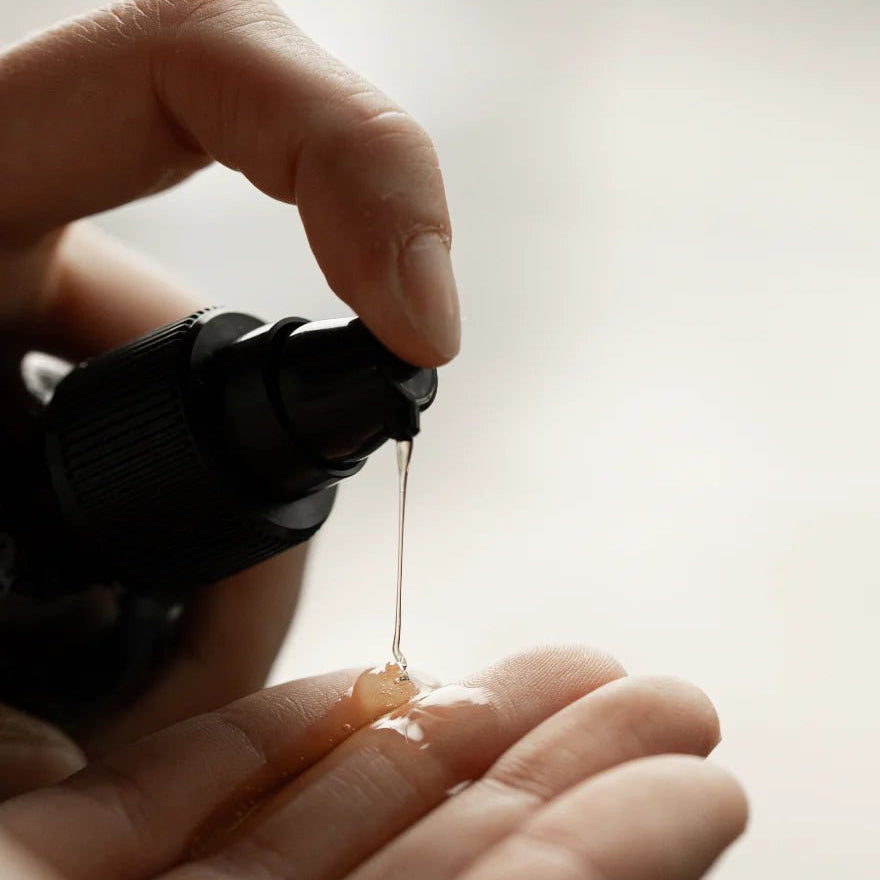 A hand dispenses Oway Silk’N Glow Serum, an anti-frizz shine serum for dry, frizzy hair, from a pump bottle onto the palm of another hand.