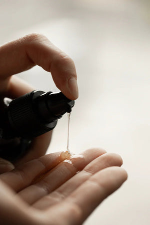 A hand dispenses Oway Silk’N Glow Serum | Anti-Frizz Shine Serum for Dry, Frizzy Hair onto another open palm. The neutral, softly blurred background keeps the focus on the Oway product in use.