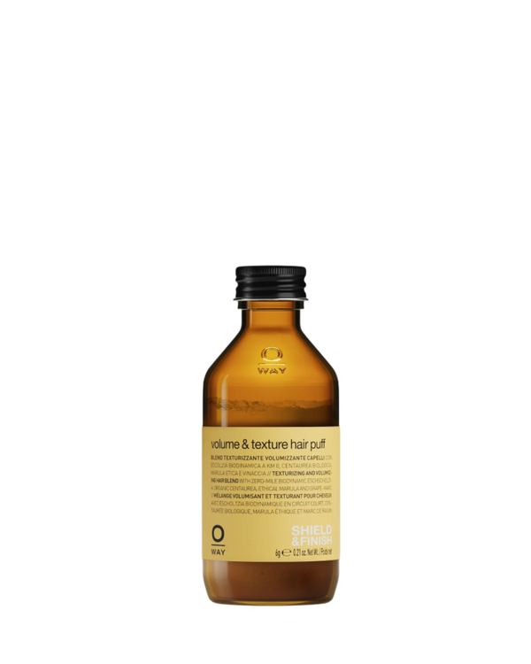A brown glass bottle with a black cap labeled “Oway Volume and Texture Hair Puff | Volumizing Styling Powder for Instant Lift” features a yellow label (100g/3.52oz) and is set against a white background.