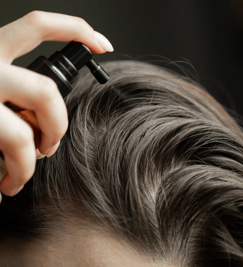 Person applying hair product to their hair with a spray bottle.