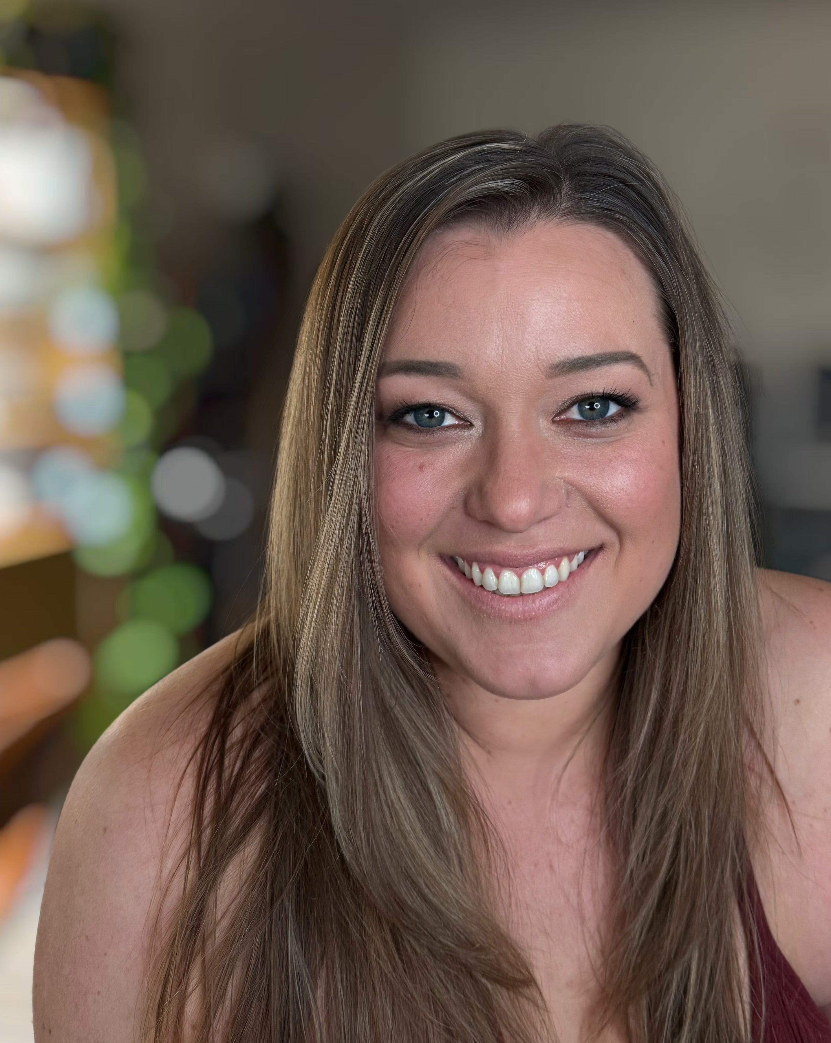 Woman with long brown hair smiling at the camera with a blurred background