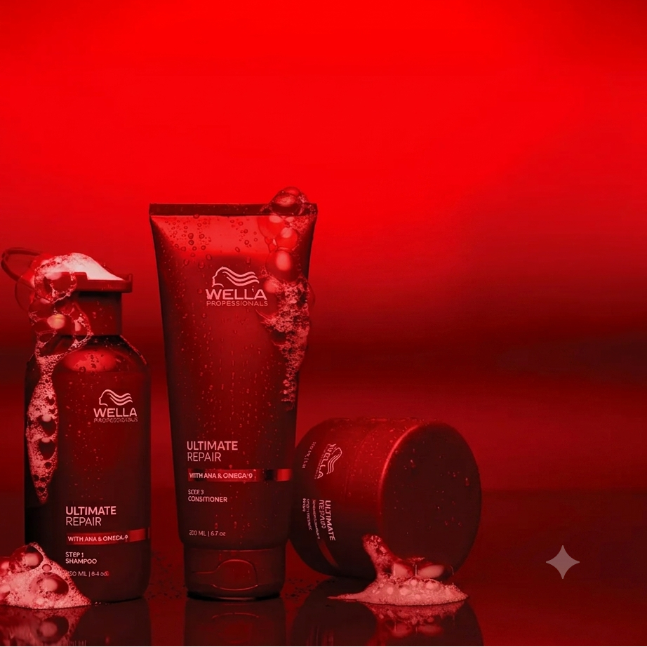 Three Wella Professionals Ultimate Repair haircare products in a dramatic red studio setup: a bottle, a tube, and a jar, with foaming product visible on the surfaces against a vivid red background.