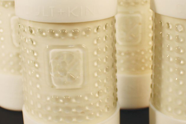 Close-up view of several Cult and King CREAM POP bottles featuring a dotted texture and a raised square emblem, partially filled with a white liquid. This silicone-free conditioning cleanser promises to deliver shiny hair with every use.