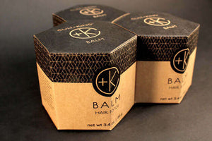 Three hexagonal cardboard boxes with black lids show the label "Cult and King BALM | Hair to Toe" and geometric patterns. These 3.4 oz boxes hold an organic, botanical balm for skin and hair care, beautifully arranged on a dark surface.
