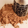 Cult and King HAIR POWDER | Dry Shampoo, Volume, Dark & Light Formulas bottle is sitting on top of a pile of brown powder.