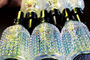 Cult and King's SUPER WATER Antioxidant Toner for Hair and Skin is displayed in clear, textured glass bottles with dark caps. Under vibrant lighting, the bottles reflect colorfully—ideal for highlighting hydration essentials.