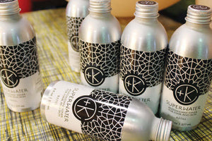 Six silver bottles of Cult and King SUPER WATER Antioxidant Toner for Hair and Skin, with black-and-white geometric labels, are displayed—perfect for hydration and a vegan lifestyle.