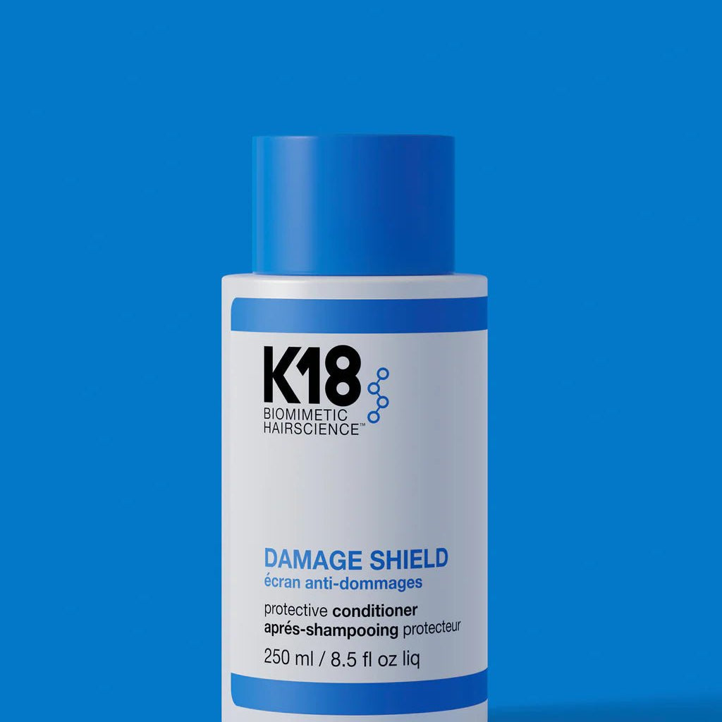 Bottle of K18 Hair Repair K18 Damage Shield pH Protective Conditioner - Multiple Sizes, a nourishing conditioner for hair health, on a blue background.