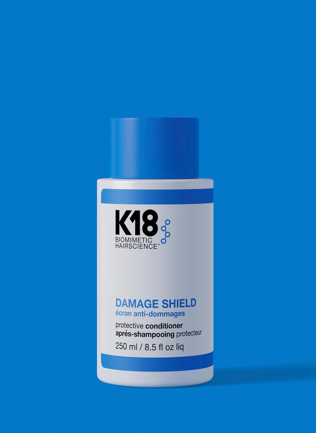 A bottle of K18 Damage Shield pH Protective Conditioner by K18 Hair Repair, a nourishing conditioner for hair health with blue and white labeling against a blue background. The bottle is 250 ml (8.5 fl oz).