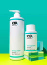A bottle of color-safe K18 PEPTIDE PREP Detox Shampoo by K18 Hair Repair and a bottle of water are placed next to each other.