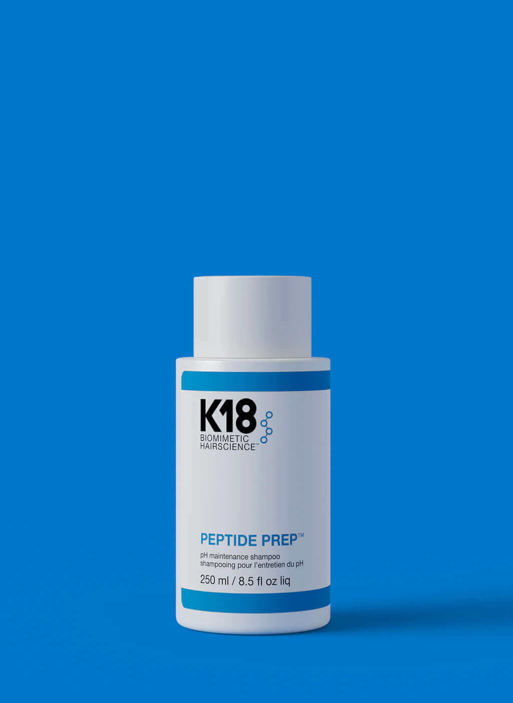 A white bottle labeled "K18 DAMAGE SHIELD pH Protective Shampoo - Multiple Sizes" stands against a blue background. This 250 ml (8.5 fl oz) cleansing shampoo, crafted with K18PEPTIDE™, is perfect for daily use to maintain optimal pH balance and hair health.