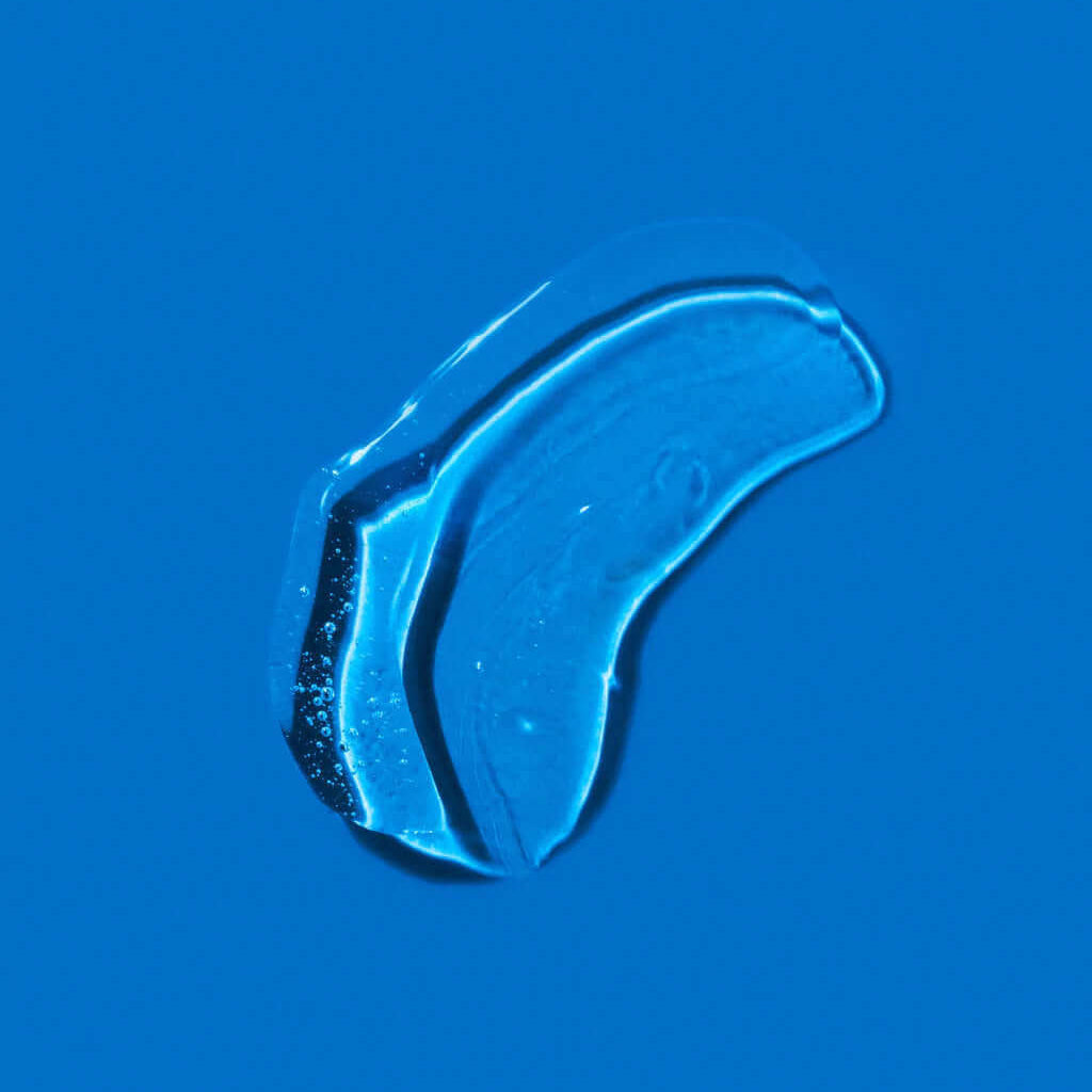 Close-up of a single clear liquid droplet on a blue surface, reminiscent of the refreshing effects of daily use with K18 DAMAGE SHIELD pH Protective Shampoo - Multiple Sizes by K18 Hair Repair.