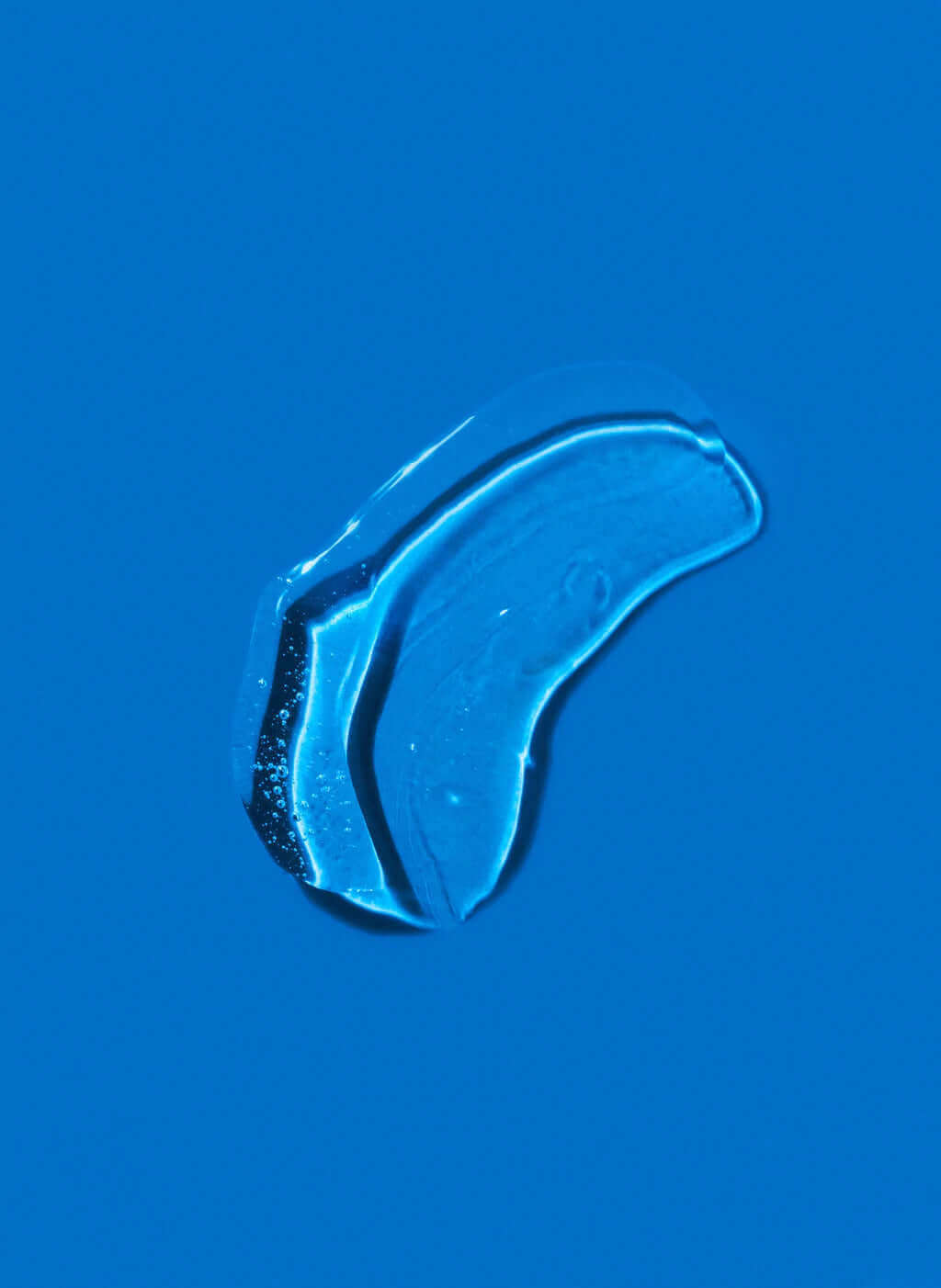 Close-up of a single clear liquid droplet on a blue surface, reminiscent of the refreshing effects of daily use with K18 DAMAGE SHIELD pH Protective Shampoo - Multiple Sizes by K18 Hair Repair.